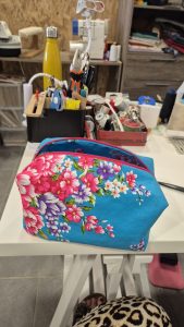 trousse fait main en tissu bleu avec motifs floraux colorés, posée sur une table d'atelier;